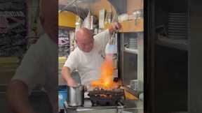 Fast-handed chef uses flamethrower to grill chicken while sprinkling on water to stoke flames